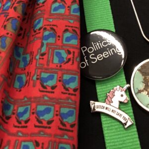 collection of conference items: green lanyard, black 'Politics of Seeing' badge, an 'Edtech will not save you' unicorn badge, and a red scarf